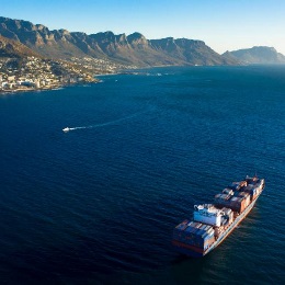 Aerial shot of a very large ship crossing the ocean with a mountain range in the background.